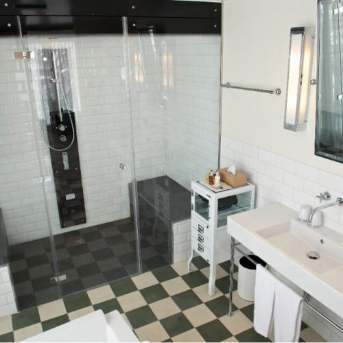 Badezimmer mit Duschbereich in dem Zementfliesen verlegt wurden (Hotel) | Unifliesen in den Farben Elfenbein (M02) und Schwarzoliv (M53) | Referenznummer: 7454
